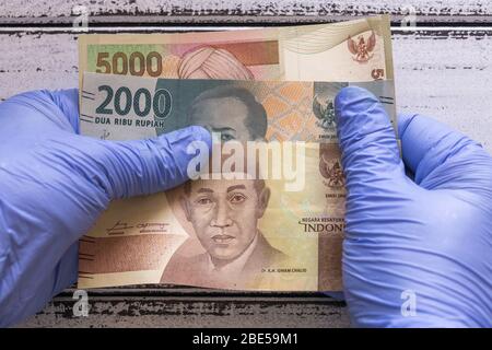 Indonesisches Geld, Banknoten in Gummihandschuhen. Das Konzept der Wirtschaft und der finanziellen Bedrohungen während der Coronavirus-Pandemie Stockfoto