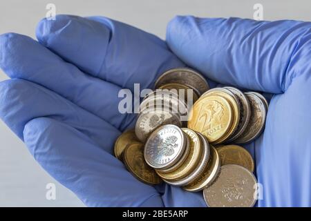 Hand in einen Gummihandschuh mit Münzen. Polnisches Geld, das Konzept der Inflation, die durch die Coronavirus-Epidemie verursacht wird Stockfoto
