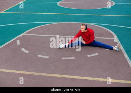 Ein junger Mann dehnt die Muskeln nach einem harten Training auf dem Sportplatz früh am Morgen. Gesundes Lifestyle-Konzept. Stockfoto