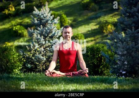 Schön fit Mann im roten Hemd meditiert auf grünem Gras im Park mit Blick auf den sonnigen Sommertagen Tag geschlossen. Konzept der Meditation und gesunde Lifestyl Stockfoto