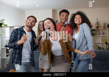 Junge asiatische Mädchen hält Mikrofon und Gesang beim Spielen Karaoke mit besten Freunden zu Hause. Gruppe von Menschen, die Spaß zusammen, trinken und Stockfoto