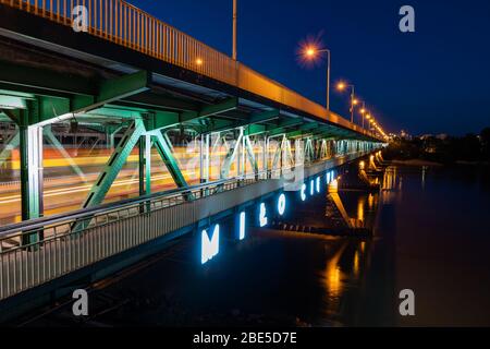 Gdanski Brücke über die Weichsel bei Nacht in Warschau in Polen, Neonschild in Polnisch - "Nice to See you", Straßenbahn-Lichtwege auf der unteren Ebene des d