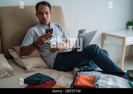 Geschäftsmann sitzt auf einem Bett und arbeitet mit Gadgets nach dem Einchecken im Hotel Stockfoto