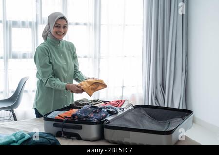 Muslimische Frauen, die Hijabs tragen, bereiten Kleidung vor einer Urlaubsreise vor, um in einen Koffer gesteckt zu werden Stockfoto