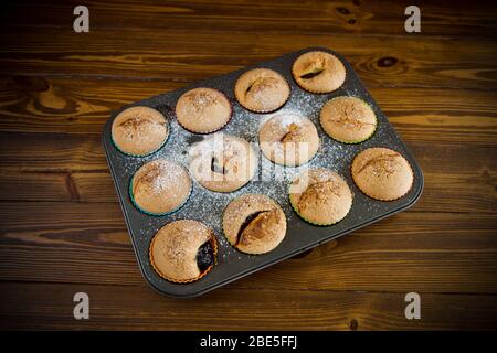 Süß gebackene Muffins mit Fruchtfüllung in Puderzucker Stockfoto