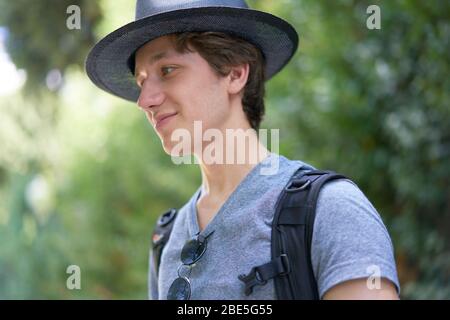 Junger schöner Mann mit Hut glücklich lächelnd in seinen Sommerferien draußen in schöner Vegetation Stockfoto
