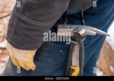 Das Arbeitswerkzeug an einer Riemenaufhängung. Betonhammer und Zange. Stockfoto