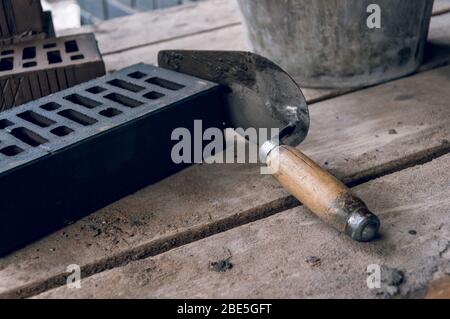 Ein Maurer-Tool durch einen strengen Plan am Arbeitsplatz. Kelle für Maurerlegung. Bau Maurer Zement Mörtel Werkzeuge. Stockfoto