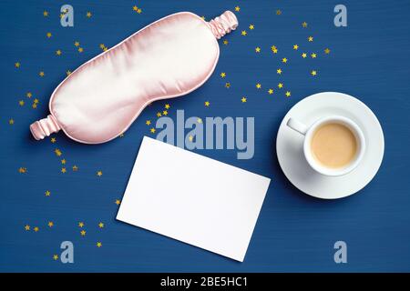 Rosa Schlafmaske, Kaffeetasse und leere Papiernotiz auf dunkelklassischem blauen Hintergrund mit Konfetti. Happy Morning, Early Wake Up, Stay Awake Concept. F Stockfoto