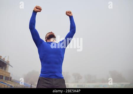 Der Kerl der Athlet hob seine Hände am Stadion im Nebel. Stockfoto