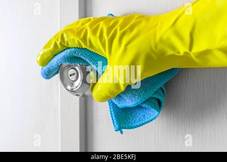 Hand des Mitarbeiters in Gummihandschuh mit Lappen, die eine Holztür abwischen. Zimmermädchen oder Hausfrau kümmert sich um das Haus. Allgemeine oder regelmäßige Reinigung der Feder. Com Stockfoto