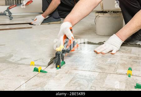 Ein Arbeiter nivelliert die Keramikfliesen mit Keilen und Clips. Stockfoto