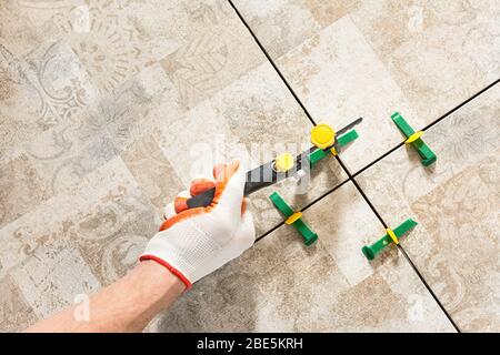 Ein Arbeiter nivelliert die Keramikfliesen mit Keilen und Clips. Stockfoto