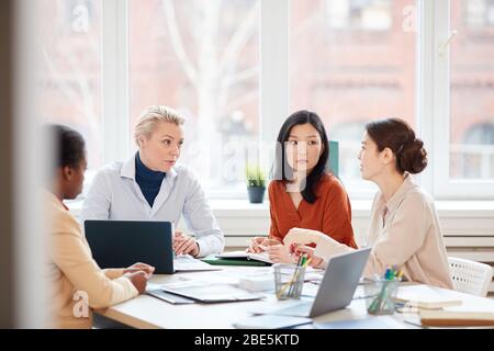 Porträt von verschiedenen weiblichen Business-Team diskutieren Projekt während des Sitzens am Tisch während der Sitzung im Konferenzraum gegen Fenster, kopieren Raum Stockfoto