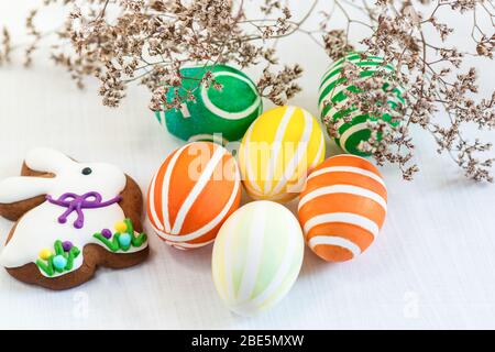 Auf dem Tisch sind leuchtend bunte Ostereier und Lebkuchen in Form eines Kaninchens. Christlicher Frühling Stockfoto