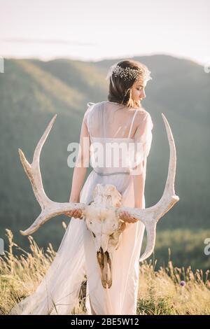 Eine schöne Braut eine Frau hält einen Elchschädel an der Hand und steht mit dem Rücken in die Berge im Sommer Stockfoto