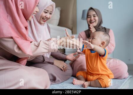 Drei muslimische Frauen spielen gern mit kleinen Jungen, wenn sie im Schlafzimmer auf dem Boden sitzen Stockfoto