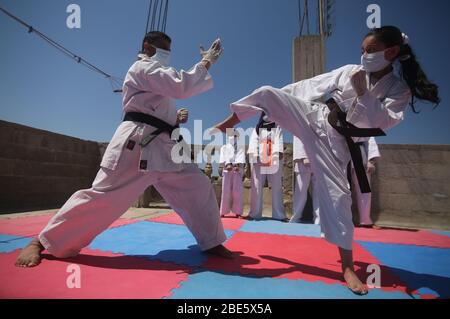 Palästina, Stadt Rafah im Gazastreifen. April 2020. Der palästinensische Karate-Ausbilder Khaled Sheikh Al-Eid (L) trainiert am 12. April 2020 mit einem seiner Kinder auf dem Hausdach in der Stadt Rafah im südlichen Gazastreifen. Kredit: Khaled Omar/Xinhua/Alamy Live News Stockfoto