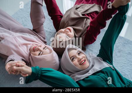 Eine Gruppe muslimischer Freundinnen lächelte, während sie auf der Matratze lagen und die Hände hielten, die nach oben schauten Stockfoto
