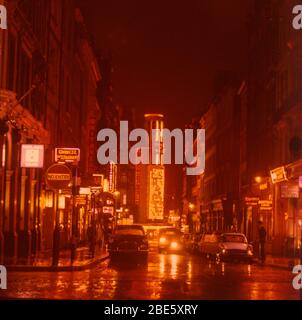 Eine Aufnahme, die 1964 bei Nacht und im Regen auf die Rupert Street in Londons Soho mit dem Prince of Wales Theatre am Ende und den Neonlichtern in den Pfützen gedreht wurde. Stockfoto