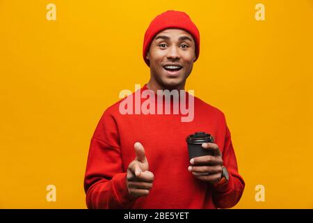 Bild eines überrascht positiven jungen afrikanischen Kerl Kaffee trinken isoliert über gelbe Wand Hintergrund zeigt auf Sie. Stockfoto