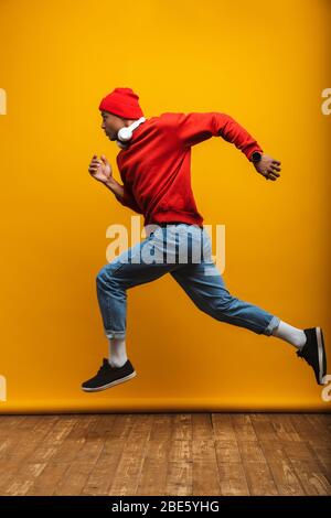 In voller Länge Seitenansicht Porträt eines attraktiven zuversichtlich lässig jungen afrikanischen Mann läuft über gelben Hintergrund Stockfoto