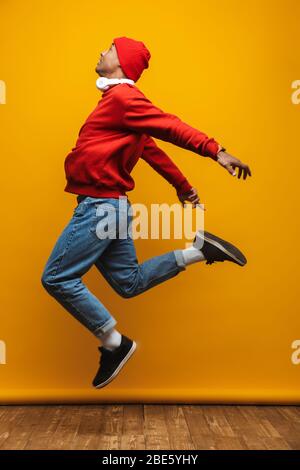 In voller Länge Seitenansicht Porträt eines attraktiven zuversichtlich lässig jungen afrikanischen Mann läuft über gelben Hintergrund Stockfoto