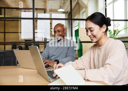 Bild von multiethnischen jungen weiblichen und männlichen Kollegen, die am Tisch sitzen und im Büro an Laptops arbeiten Stockfoto