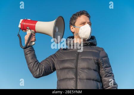 Der junge Mann hört neue Informationen und Nachrichten aus dem Megaphon über die Coronavirus-Epidemie in der Welt Stockfoto