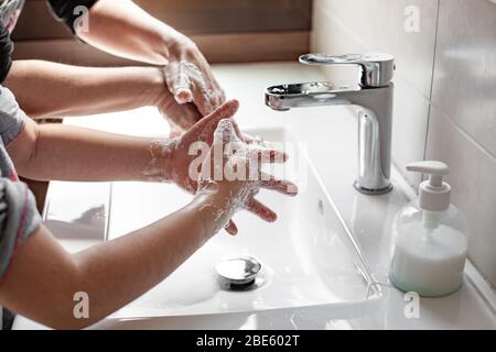 Mutter lehrt ihre Tochter, wie man ihre Hände richtig mit Seife waschen, um eine Coronavirus-Infektion zu verhindern Stockfoto