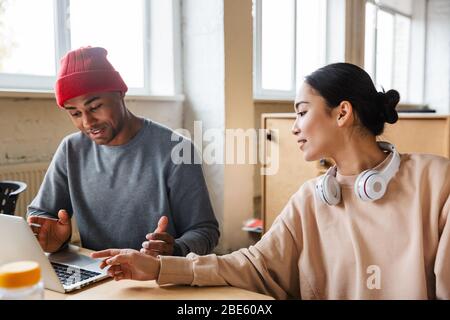 Bild von multiethnischen jungen weiblichen und männlichen Kollegen, die am Tisch sitzen und im Büro an Laptops arbeiten Stockfoto