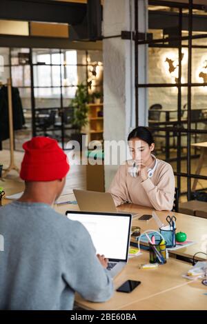 Bild von multiethnischen jungen weiblichen und männlichen Kollegen, die am Tisch sitzen und im Büro an Laptops arbeiten Stockfoto