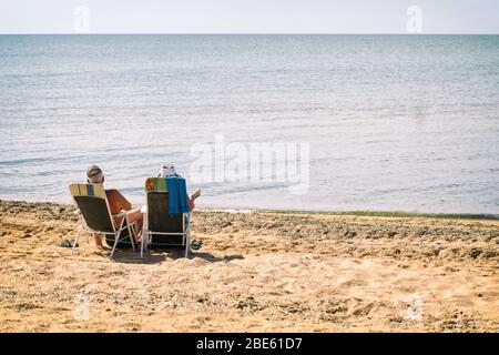 Ältere Paare sitzen am Strand am Meer Stockfoto