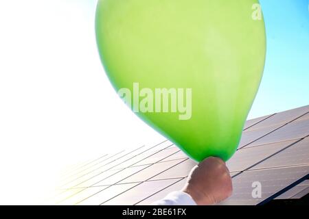 Neue Generationen streben danach, Solarenergie zu nutzen. Das Kind hält eine grüne Kugel auf dem Hintergrund von Solarmodulen. Stockfoto