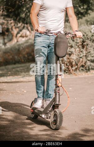 Mann mit Roller. Anonymer Athlet Mann Reiten Elektroroller entlang Weg an sonnigen Herbsttag in der Stadt. Stockfoto