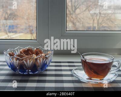 Auf der Fensterbank befindet sich eine transparente Tasse Tee und eine Schüssel Bagels. Unterhaltung in Isolation. Stillleben. Stockfoto