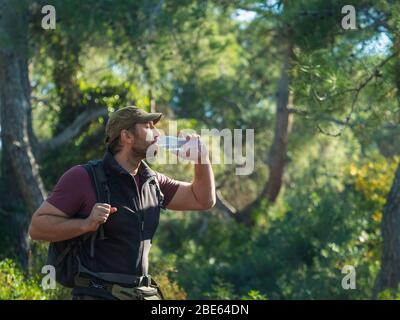 Männliche Touristen trinken klares Wasser aus einer Flasche im Wald. Reise, aktives und gesundes Lifestyle-Konzept. Stockfoto