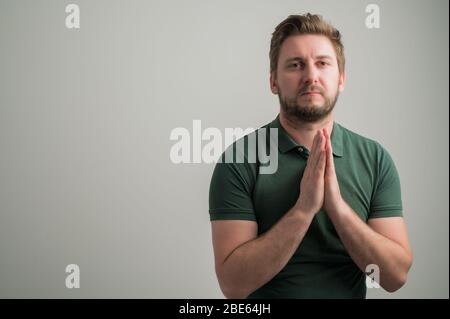 Porträt von seriösen stilvollen attraktiven Mann mit dicken Bart, in lässigen grünen T-Shirt gekleidet ist beten isoliert auf grauem Hintergrund mit Kopie Raum Anzeige Stockfoto