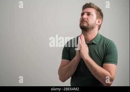 Porträt von seriösen stilvollen attraktiven Mann mit dicken Bart, in lässigen grünen T-Shirt gekleidet ist beten isoliert auf grauem Hintergrund mit Kopie Raum Anzeige Stockfoto