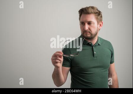 Porträt von seriösen stilvollen attraktiven Mann mit dicken Bart, in lässig grün T-Shirt gekleidet Blick auf die Brille auf grauem Hintergrund mit Kopie isoliert Stockfoto