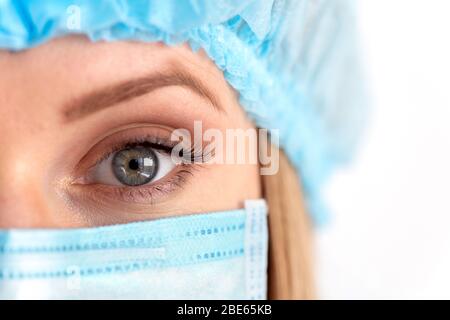 Nahauge des weiblichen Chirurgenarztes bei Erwachsenen, der eine Schutzmaske und eine Schutzkappe trägt. Konzept für das Gesundheitswesen, den medizinischen Notfalldienst und die Chirurgie Stockfoto