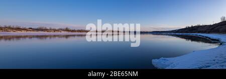 Panoramablick auf den Sonnenuntergang am Flussufer des South Saskatchewan River in den Saskatchewan Prairies während der Frühjahrssaison Stockfoto