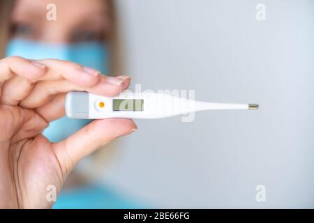 Ein weiblicher Arzt oder eine Krankenschwester hält ein elektronisches Thermometer zur Temperaturmessung. Schärfentiefe mit Fokus auf Thermometer Stockfoto