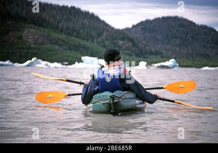 Mutter und Sohn in warmen Jacken, Hüten und Rettungswesten paddeln an einem Sommertag mit dem Kajak an Eisbergen in Halibut Cove, Homer, Alaska, USA vorbei. Stockfoto