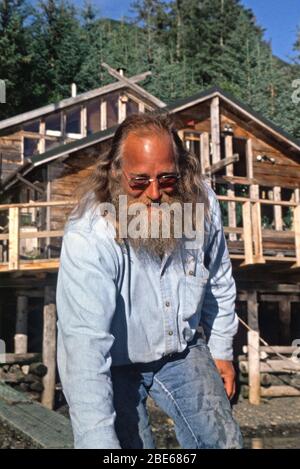 Senior Mann mit langem Bart hält ein Boot vor einer Holzhütte, Sadie Cove, Homer, Alaska, USA Stockfoto