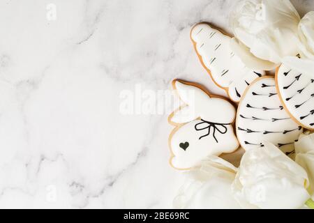 OsterLebkuchen in Form von Karotten und Kaninchen mit Bouquet von weißen Tulpen auf Marmortisch. Frohes Osterkonzept. Minimalismus Hintergrund, Draufsicht Stockfoto