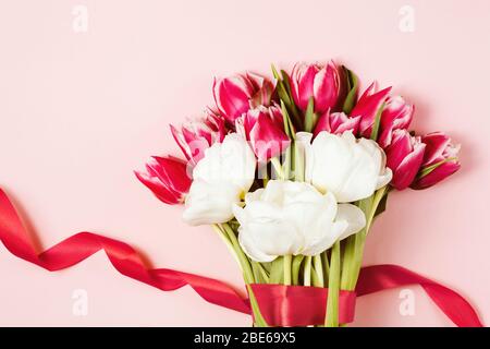 Bund rosa und weiß Pfingstrosen Tulpen mit einem roten Band auf rosa Hintergrund gebunden. Mutter und Frauen dan Konzept. Draufsicht, Kopierbereich Stockfoto