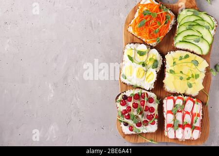 Sechs Sandwiches auf Toast mit frischen Karotten, Gurken, Ananas, rotem Currant, Krabbenstäbchen und Wachteleiern mit Erbsen Mikrogrün auf Holzbrett Stockfoto