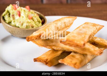 Lateinamerikanische Häppchen namens Tequenos aus frittiertem, mit Käse gefülltem Wonton und mit Guacamol serviert Stockfoto