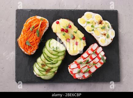 Fünf Sandwiches auf Toast mit frischen Karotten, Gurken, Ananas, rote Johannisbeere, Krabbenstäbchen und Wachteleier mit Erbsen Microgreens auf einem Schiefer stehen auf einem Stockfoto